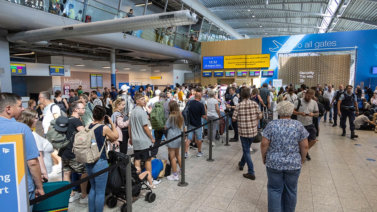 Eindhoven Airport terminal crowded with passengers sitting on luggage and security bins