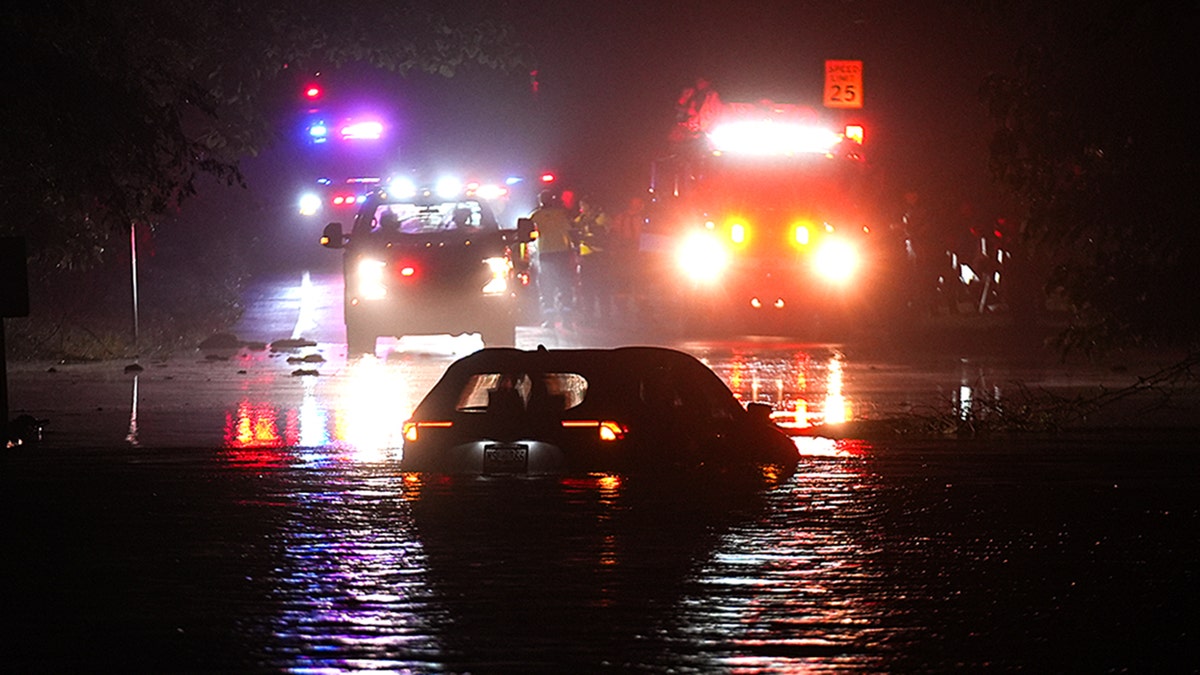 A car submerged in water with emergency response vehicles in front of it