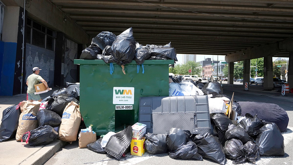 A man throws garbage into an overflowing dumpster
