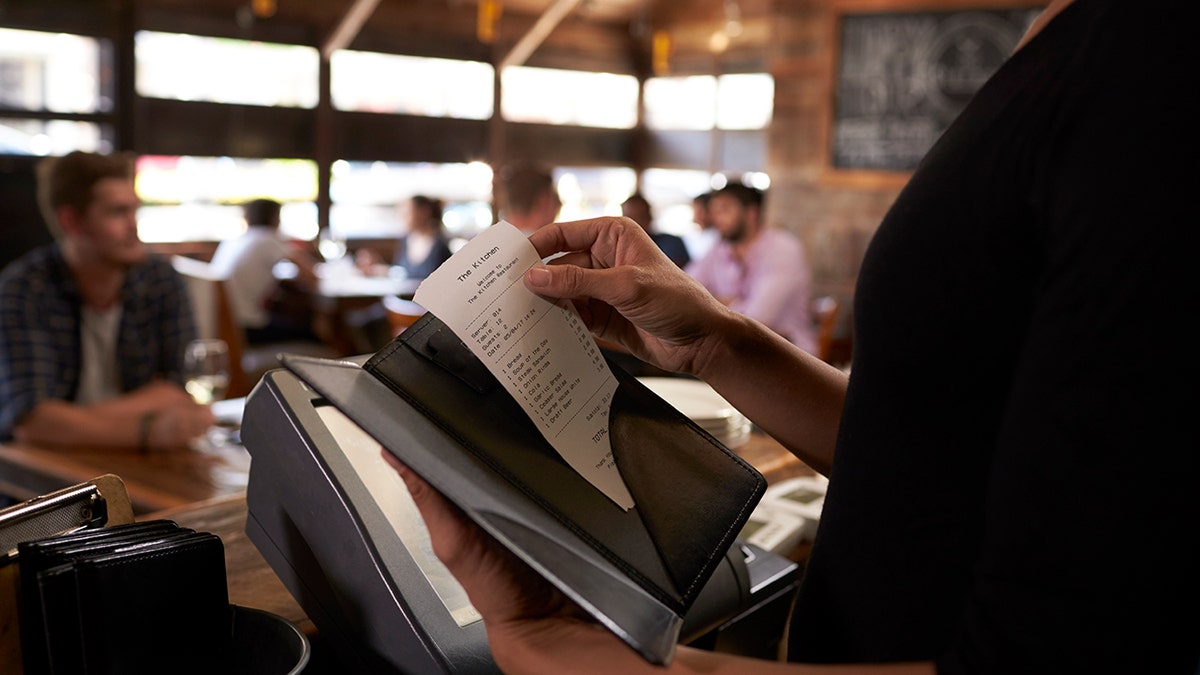 A server prepares a restaurant bill to be delivered to a table.