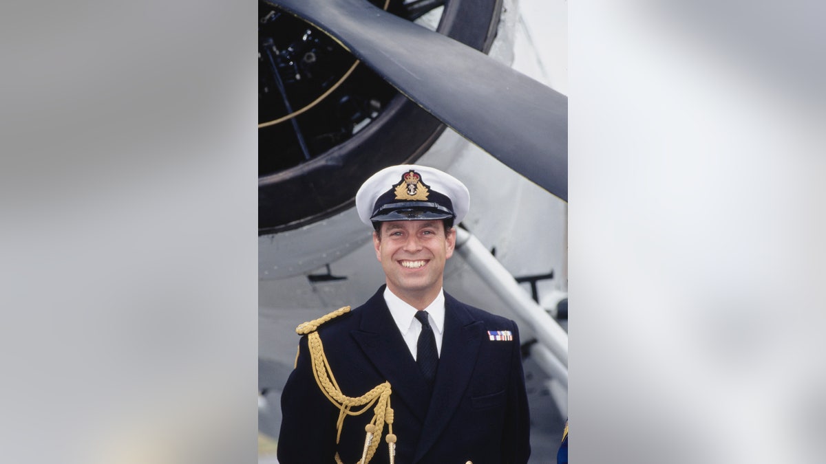 Prince Andrew in a uniform smiling in front of a plane.