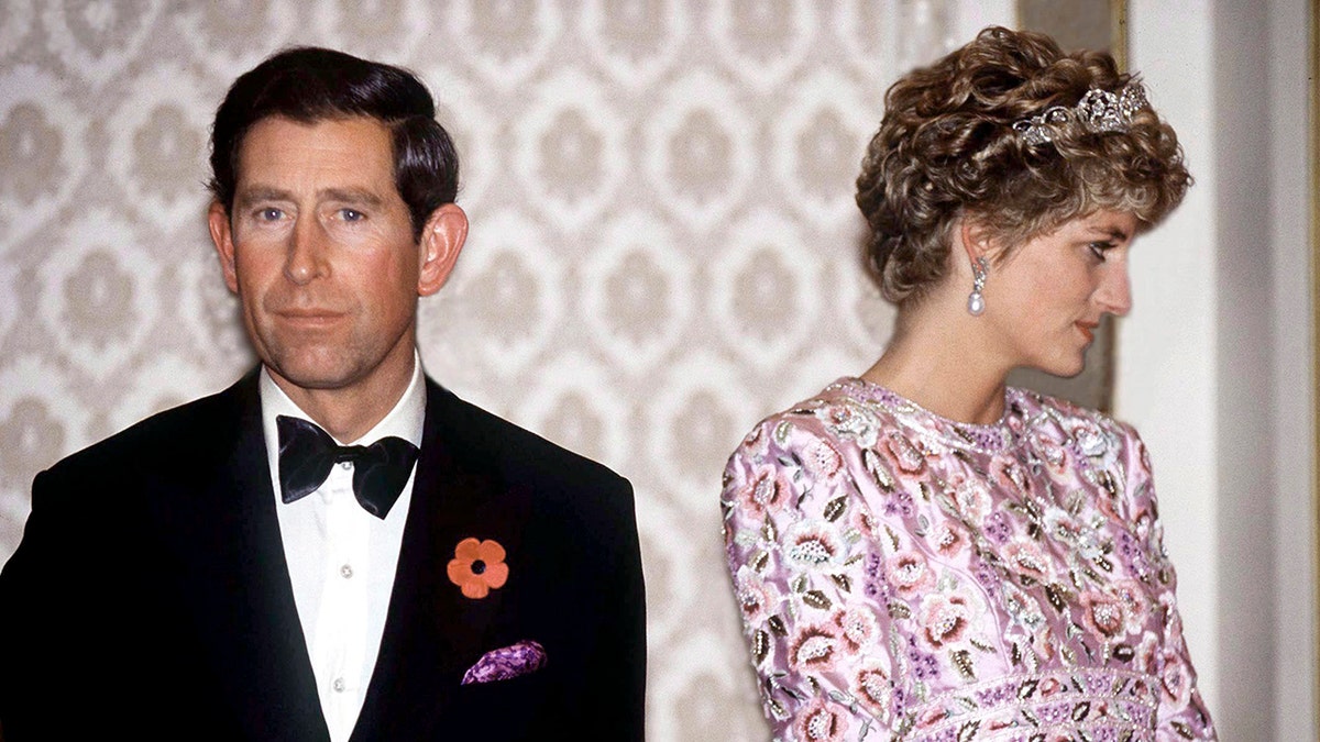 Princis Čārlzs skatās uzvalkā ar princesi Diānu, kas valkā rozā dzirkstošo kleitu un Tiara, skatoties uz sāniem.
