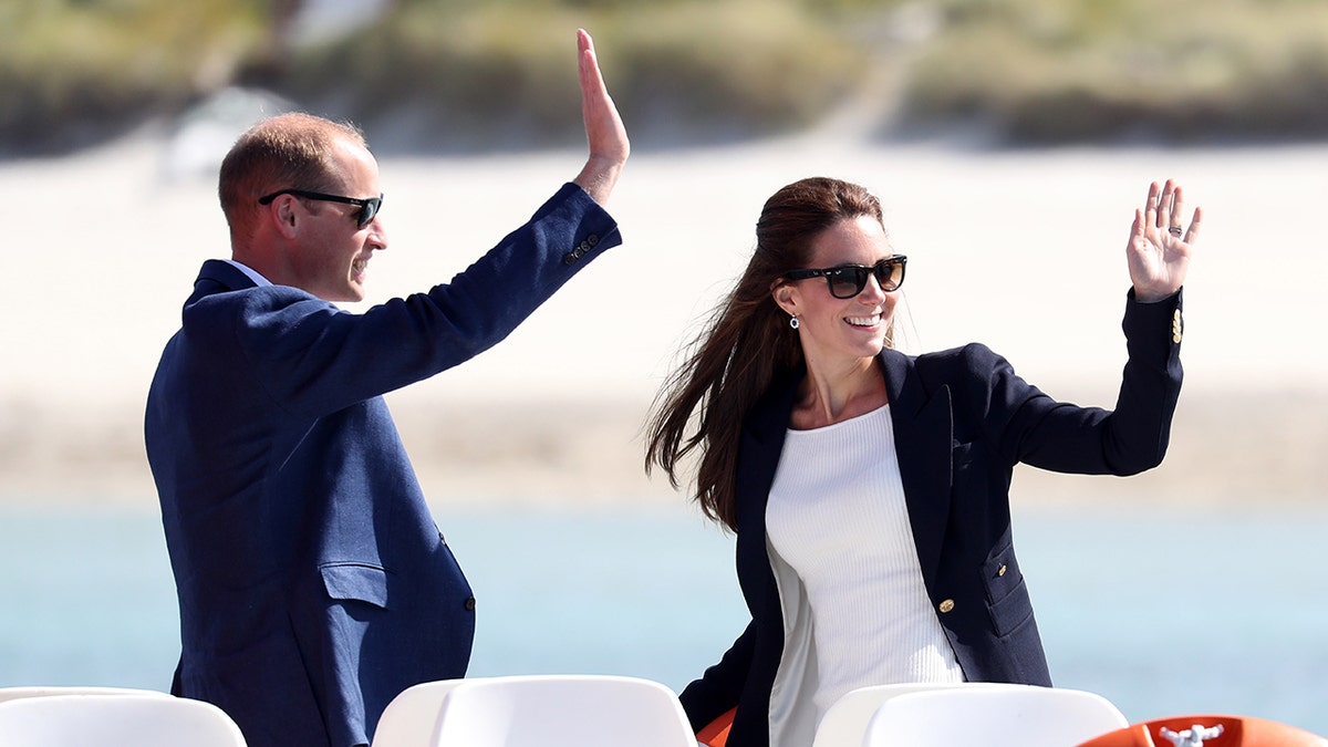 Prince William and Kate Middleton waving near a beach.
