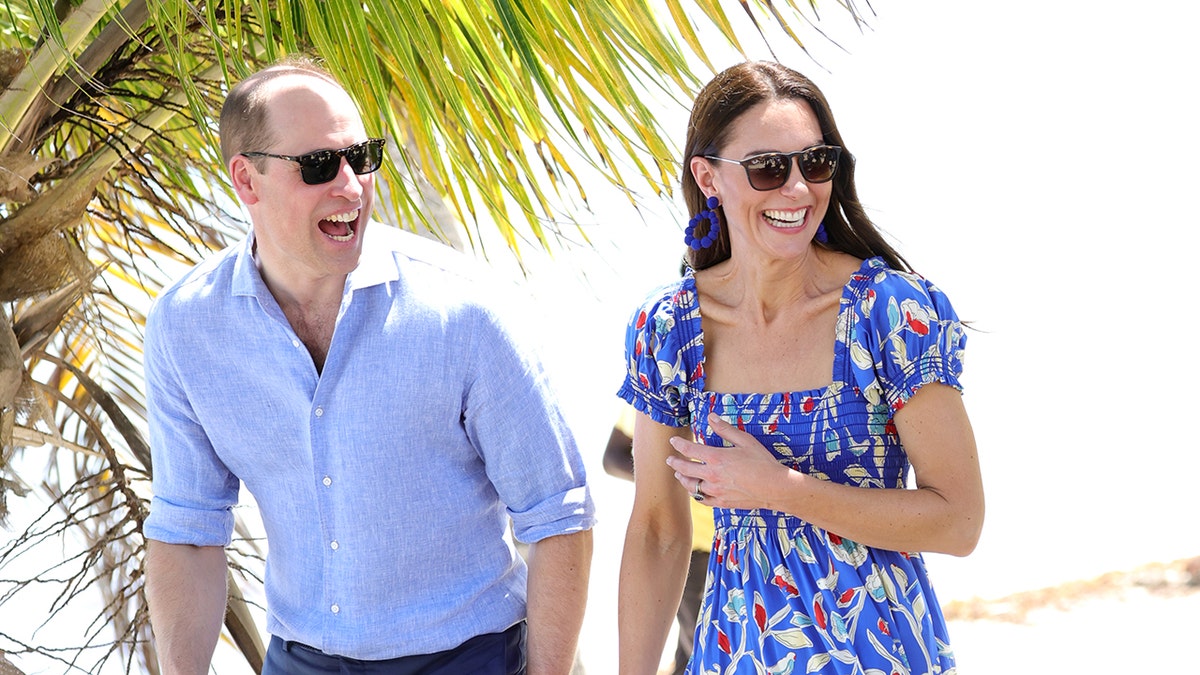 Prince William and Kate Middleton wearing blue ensembles with sunglasses smiling.