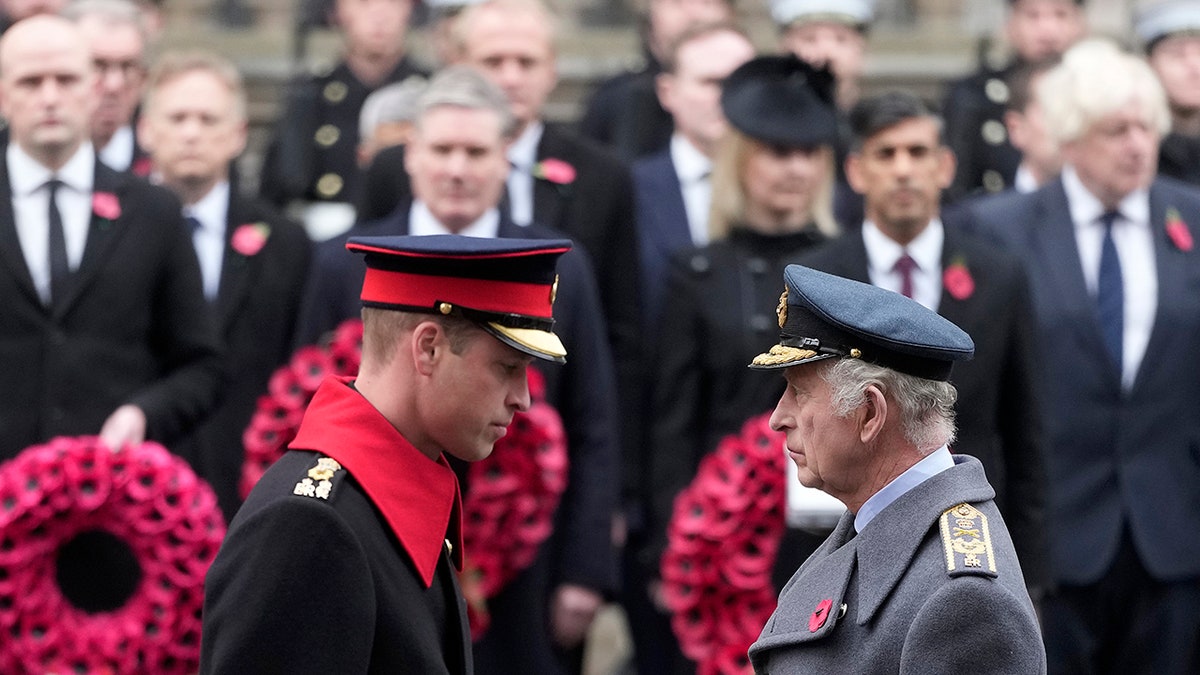 King Charles and Prince Harry in uniforms looking somber while facing each other in front of a red wreath.