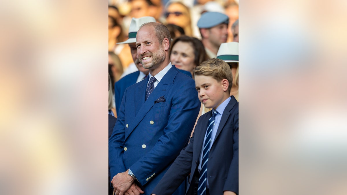 Prince William in a blue suit smiling and standing next to his son Prince George.