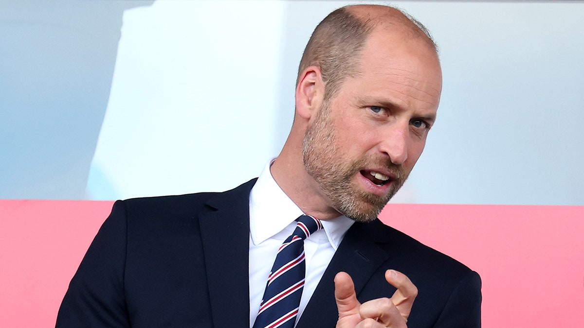 Prince William in mid conversation wearing a black blazer and a striped tie.