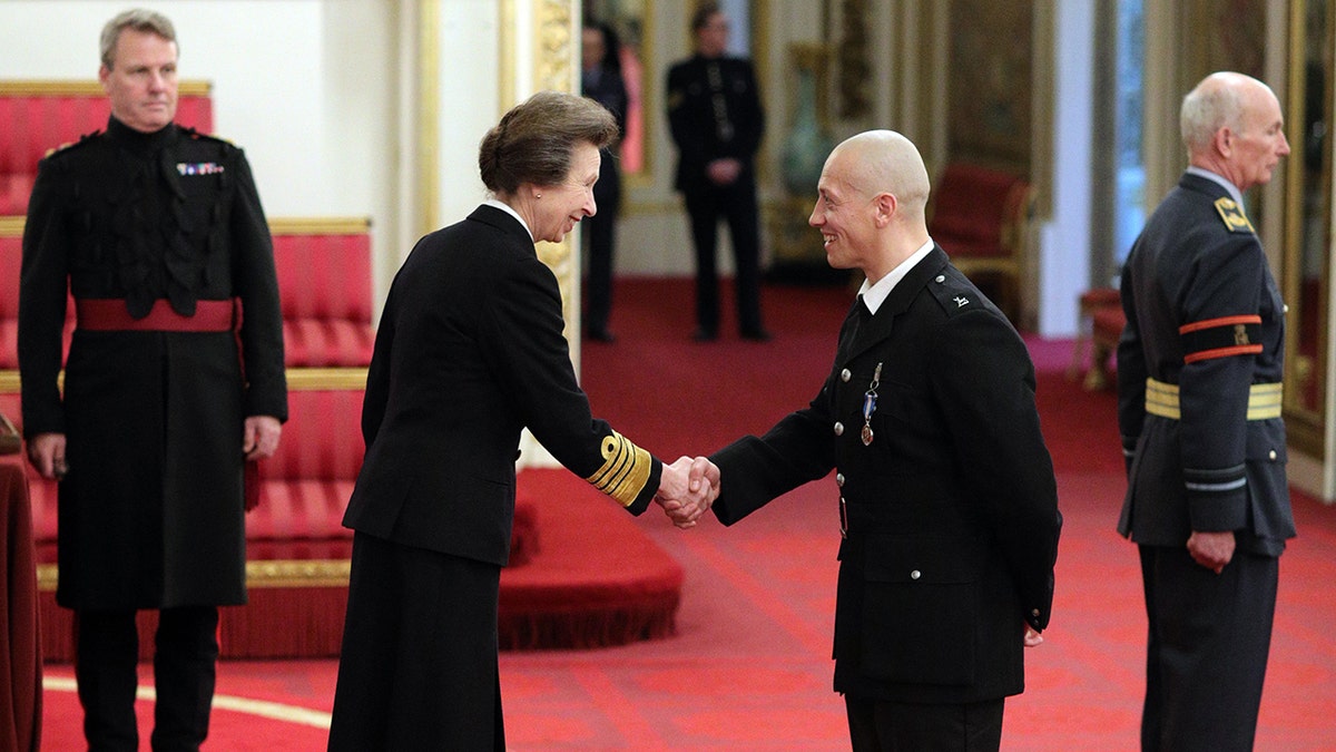 Princess Anne in a black suit shaking a man's hand in a similar looking suit.