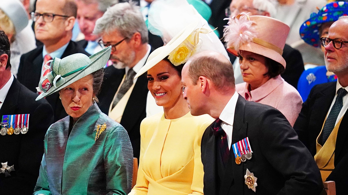 Princess Anne, Kate Middleton and Prince William sitting next to each other talking and smiling.