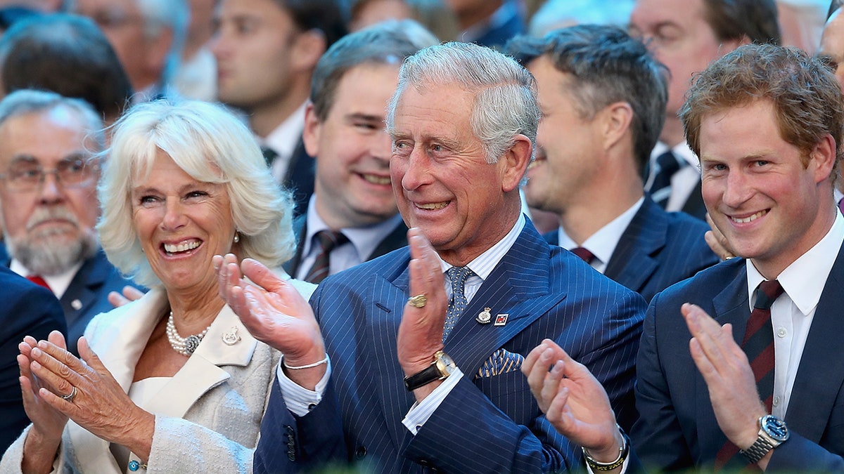 Queen Camilla, King Charles and Prince Harry in formal wear applauding.