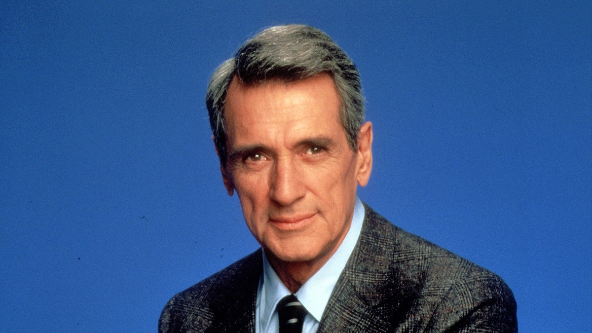 Rock Hudson in a grey suit and white shirt with black tie.