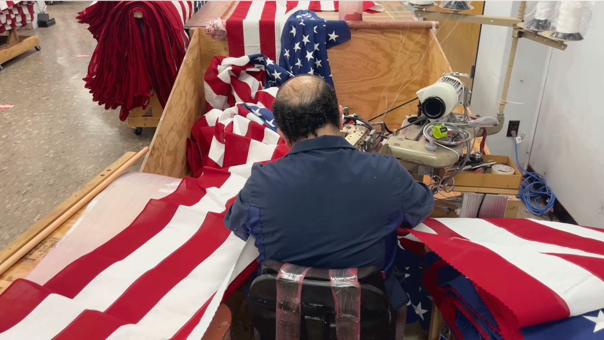 Man sewing nan apical conception of reddish and achromatic stripes to nan bottommost half of an American emblem astatine Allied Materials.