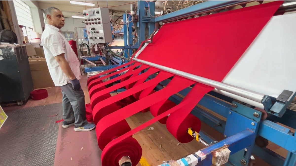 Machine cutting strips of reddish fabric cloth astatine Allied Materials