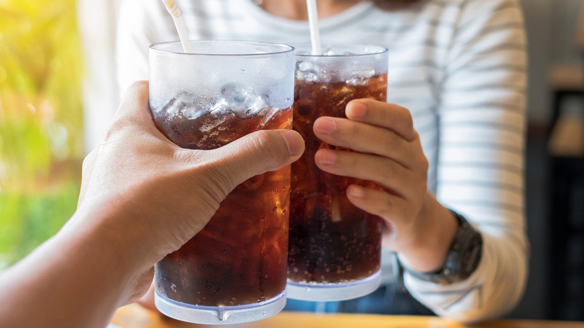 Two people clinking soda glasses