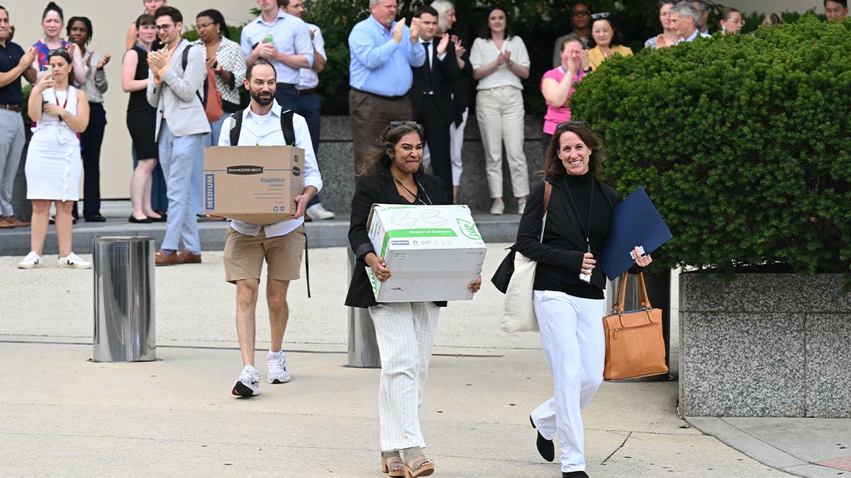 Laid-off State Department workers carry boxes out of Foggy Bottom headquarters during mass July 2025 federal downsizing.