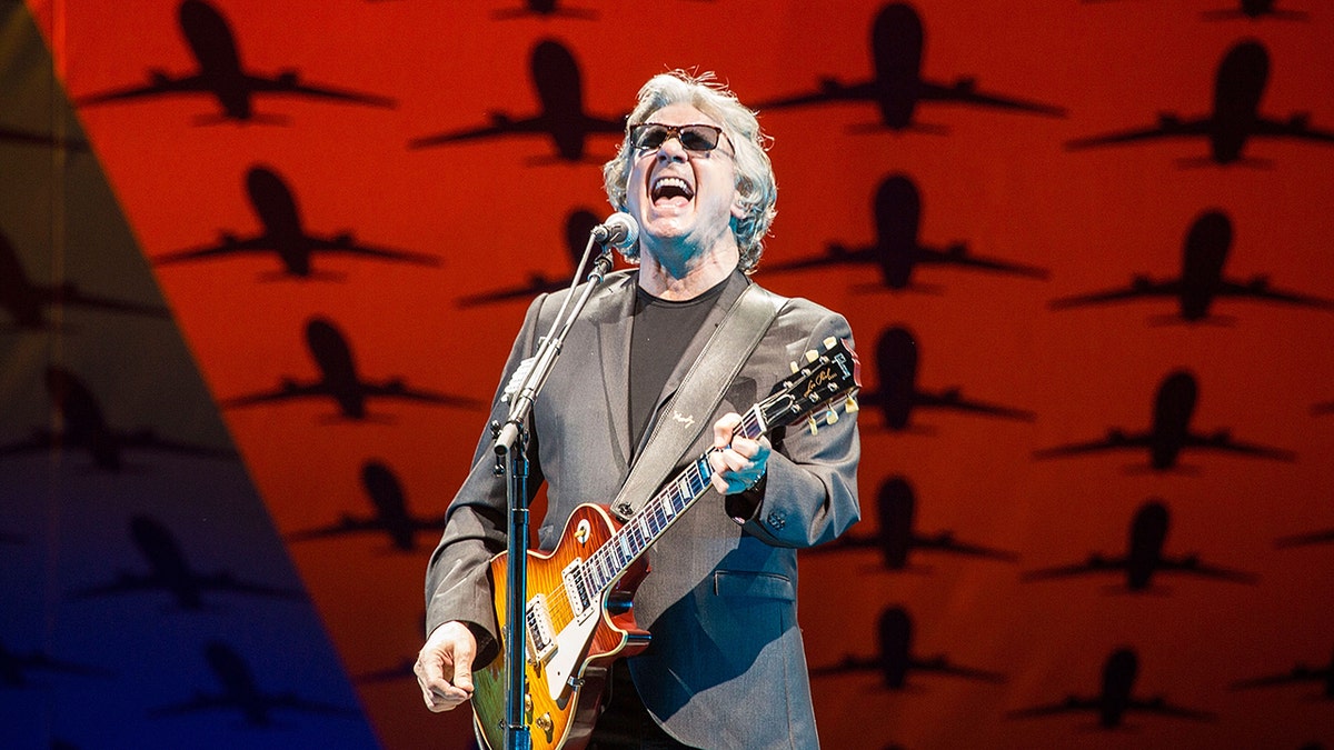 Steve Miller carries guitar during concert.