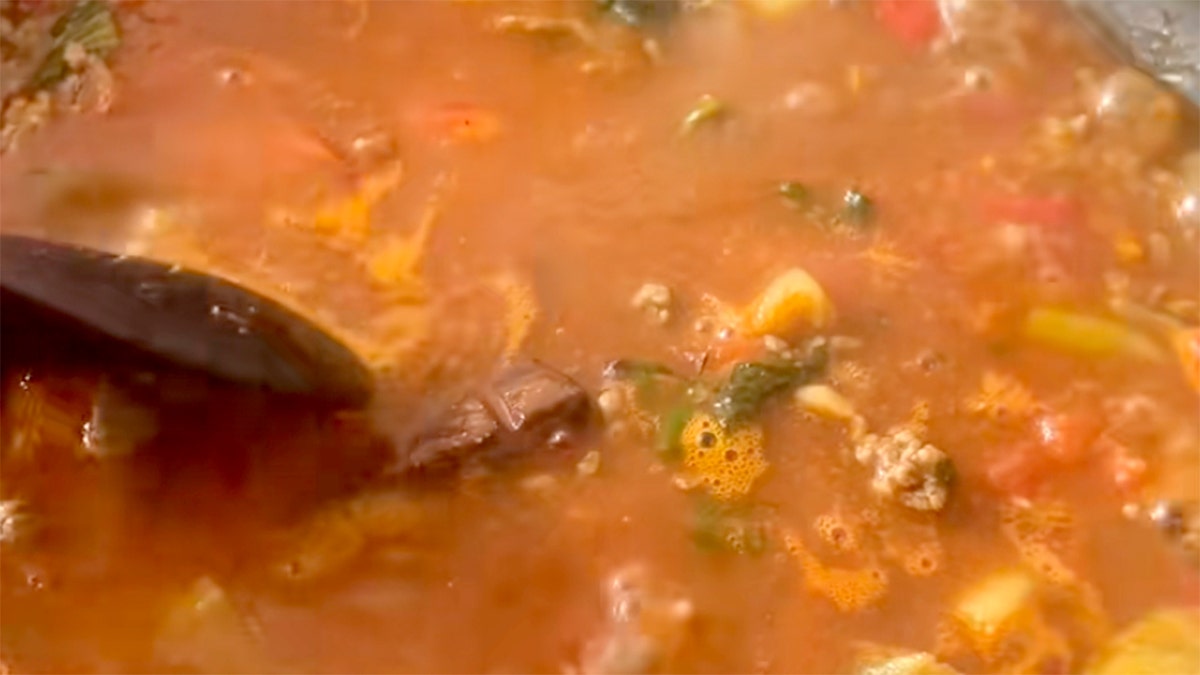 A still from a TikTok video shows a stirring spoon mixing dark chocolate into a pot of chili.
