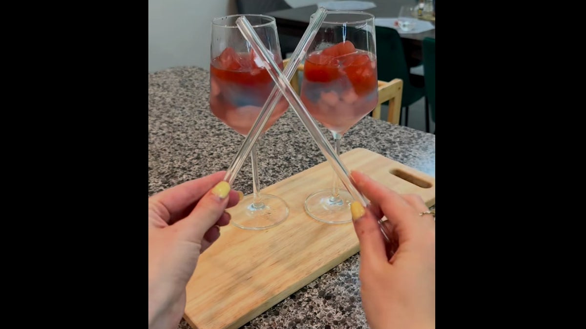 Screenshot of TikTok video showing 2 red, achromatic and bluish drinks successful vino glasses, pinch woman's hands holding straws successful beforehand of them getting fresh to service them.