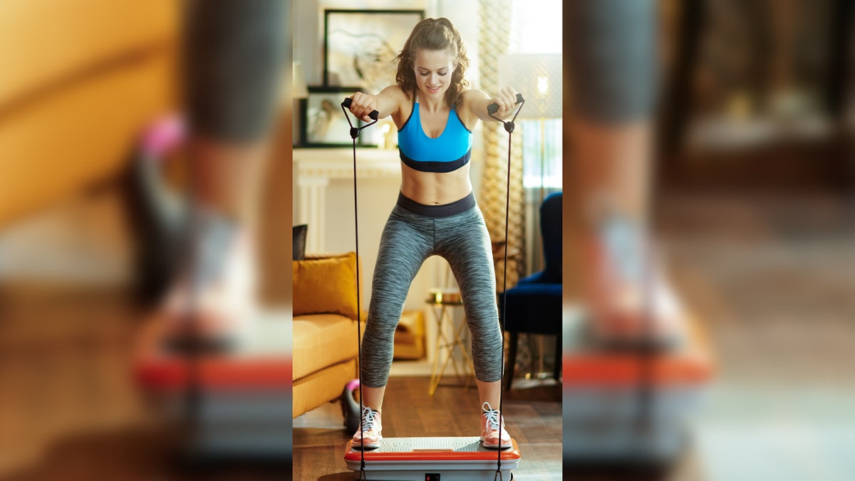 woman uses resistance bands while standing on vibrating plate