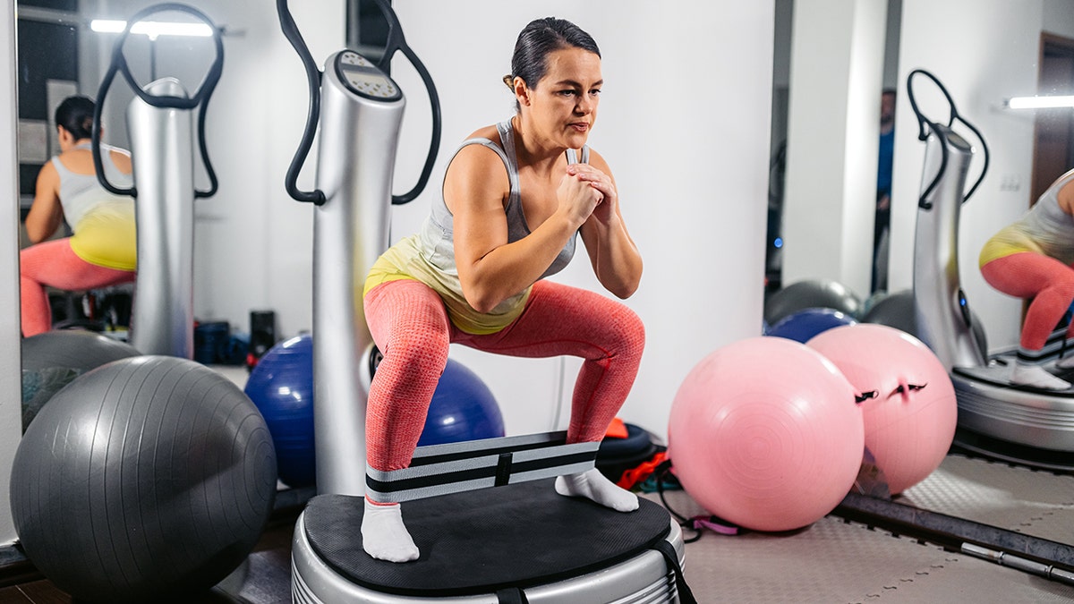 woman training with a resistance band on a vibration power plate in the gym