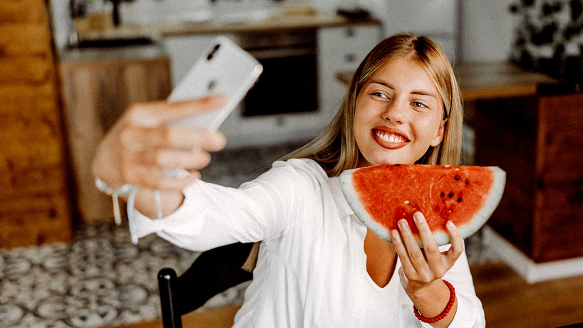 A woman takes a personal photo while eating watermelon
