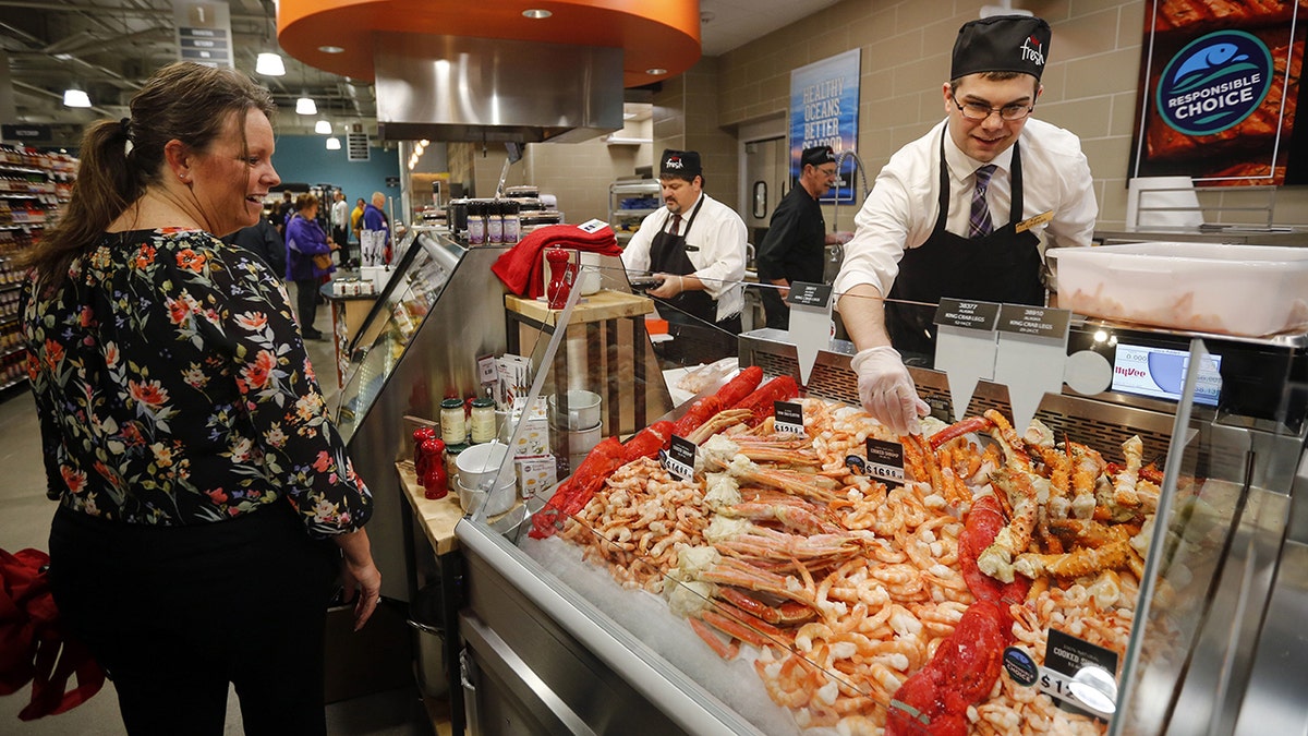 A shopper admires the seafood at Hy-Vee as an employee adjusts the signage inside the seafood case.