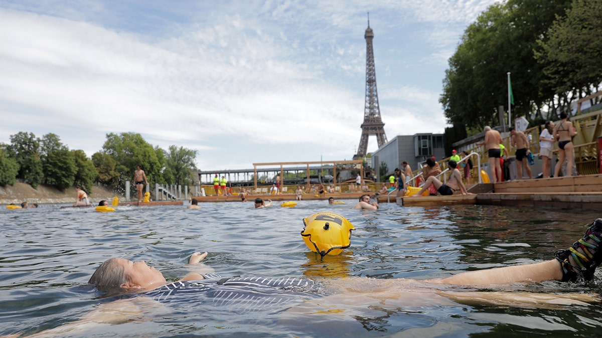 a woman swims in the seine river overlooking the Eiffel tower
