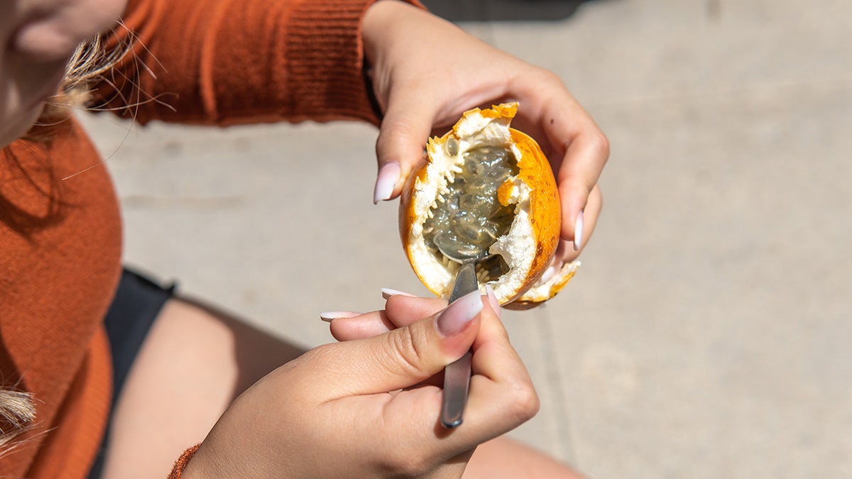 Close-up of a woman's hands as she scoops a passion fruit with a spoon