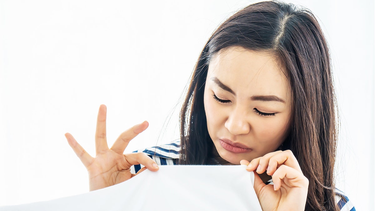 Woman sniffing pillow, making a face indicating it has a bad odor