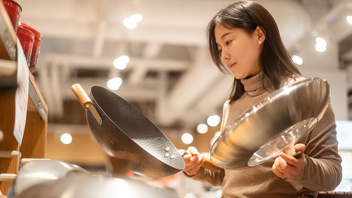 Woman looking at pans in store, holding one in each hand while she examines one