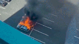 A silver vehicle exploding into a fireball in a parking lot