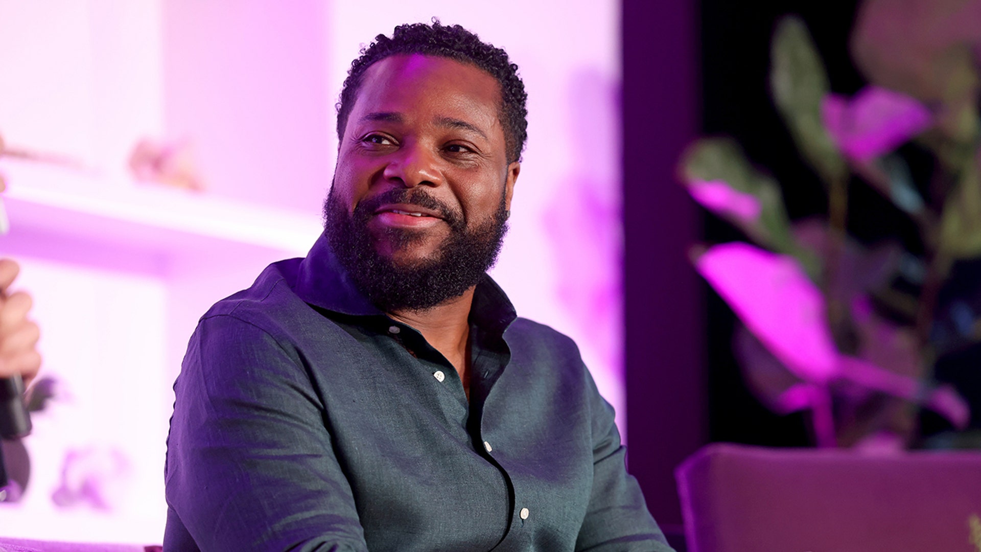 Malcolm-Jamal Warner wears a black shirt on stage during panel discussion.
