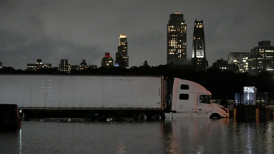 A semi-truck submerged in water in front of buildings