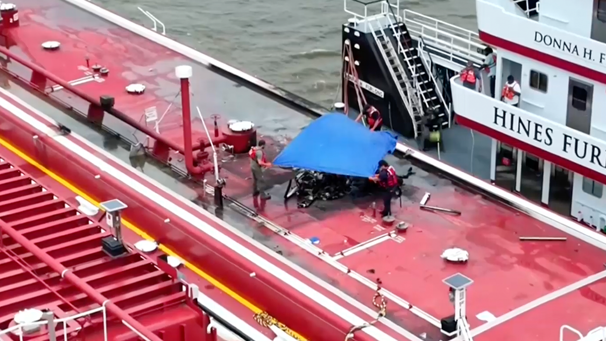 As equipes cobriram o helicóptero mutilado depois que ele caiu em uma barcaça do rio Mississippi na quinta -feira.