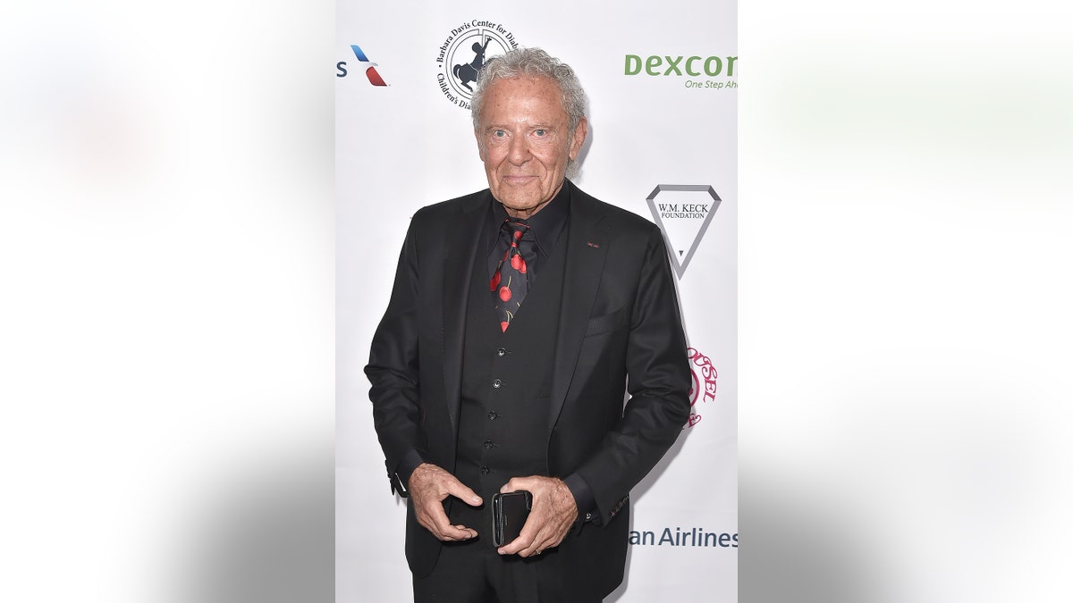 Alan Hamel, Suzanne Somers' widower, is seen wearing a dark suit smiling with a cherry printed tie.
