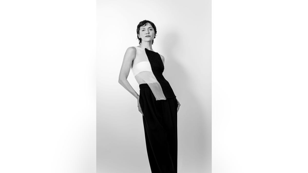 Alyon Stoner穿著一件白色的黑色和白色剪裁連衣裙，其姿勢像高級時裝模型。