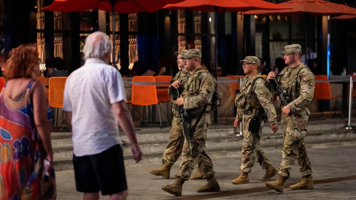 Four National Guard soldiers carrying rifles patrol a nightlife district in Washington, D.C., at night.