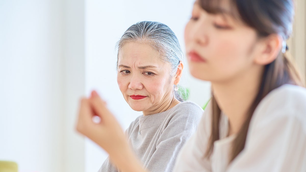Asian senior woman looking at a young woman with a grim expression