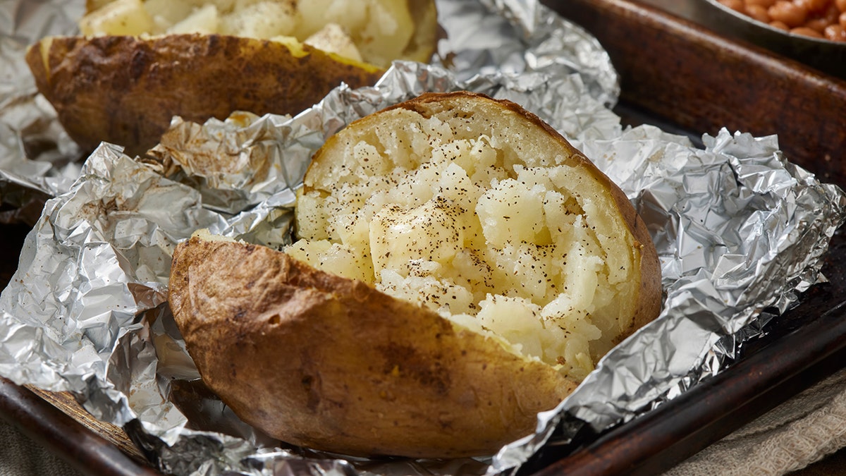 Baked potatoes seen cooked and cut open, seasoned, on tin foil