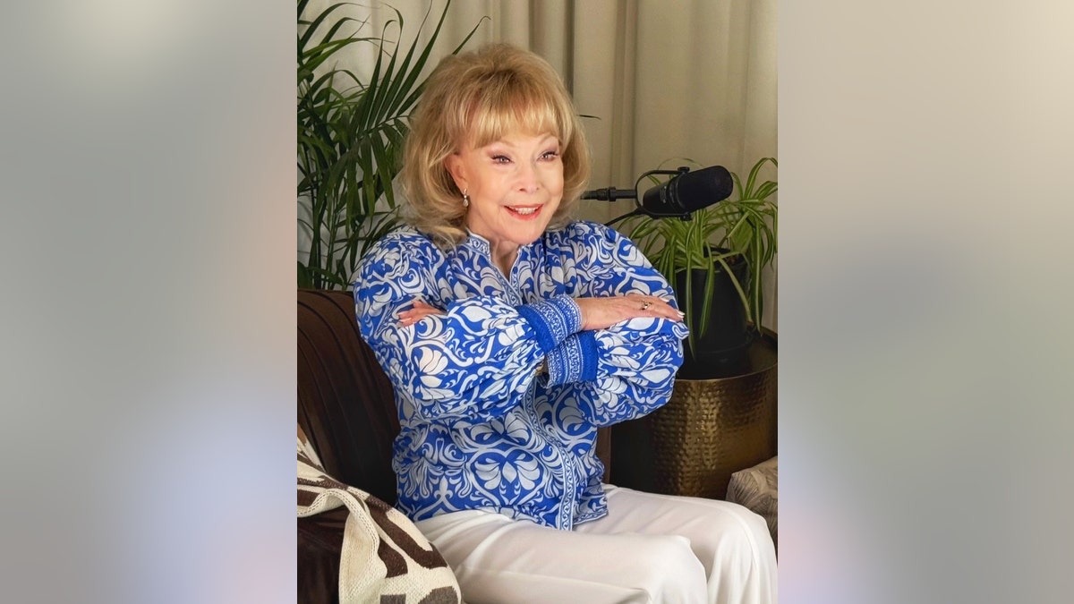 Barbara Eden wearing a blue and white printed shirt striking her signature genie pose.