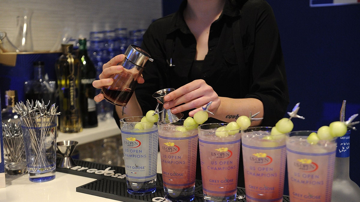 Bartender making Grey Goose Honey Deuce cocktails, four lined up in a row as she pours raspberry liquor into the last one