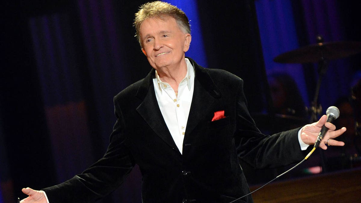 Bill Anderson with his arms outstretched on stage at the Grand Ole Opry. 