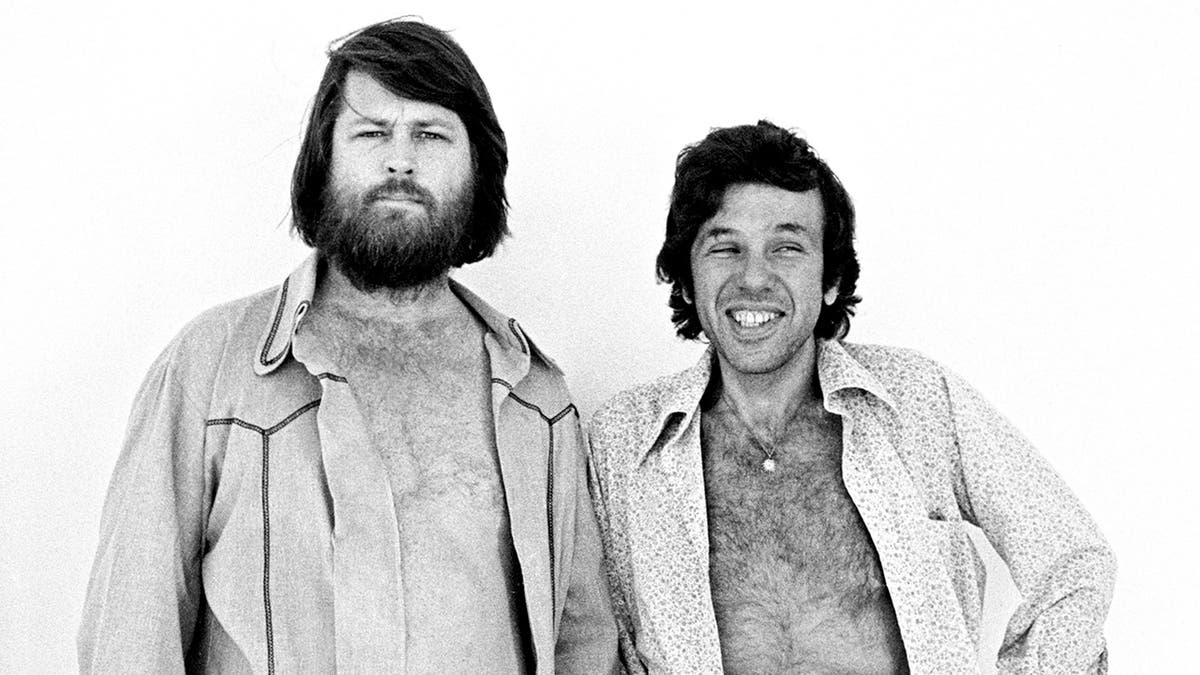 布萊恩·威爾遜（Brian Wilson）的襯衫在尤金·蘭迪（Eugene Landy）博士旁邊打開，他的襯衫也微笑著。