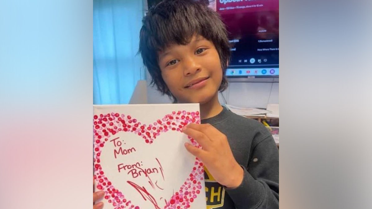 Bryan Vasquez posing with a heart-shaped card that reads: "To Mom, From Bryan"