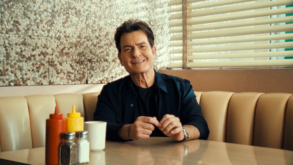 Charlie Sheen sits at a diner booth