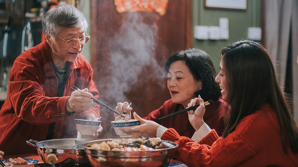 Father-in-law passing food to daughter in law during Chinese New Year family reunion dinner hong kong multi generation family having family reunion dinner at home