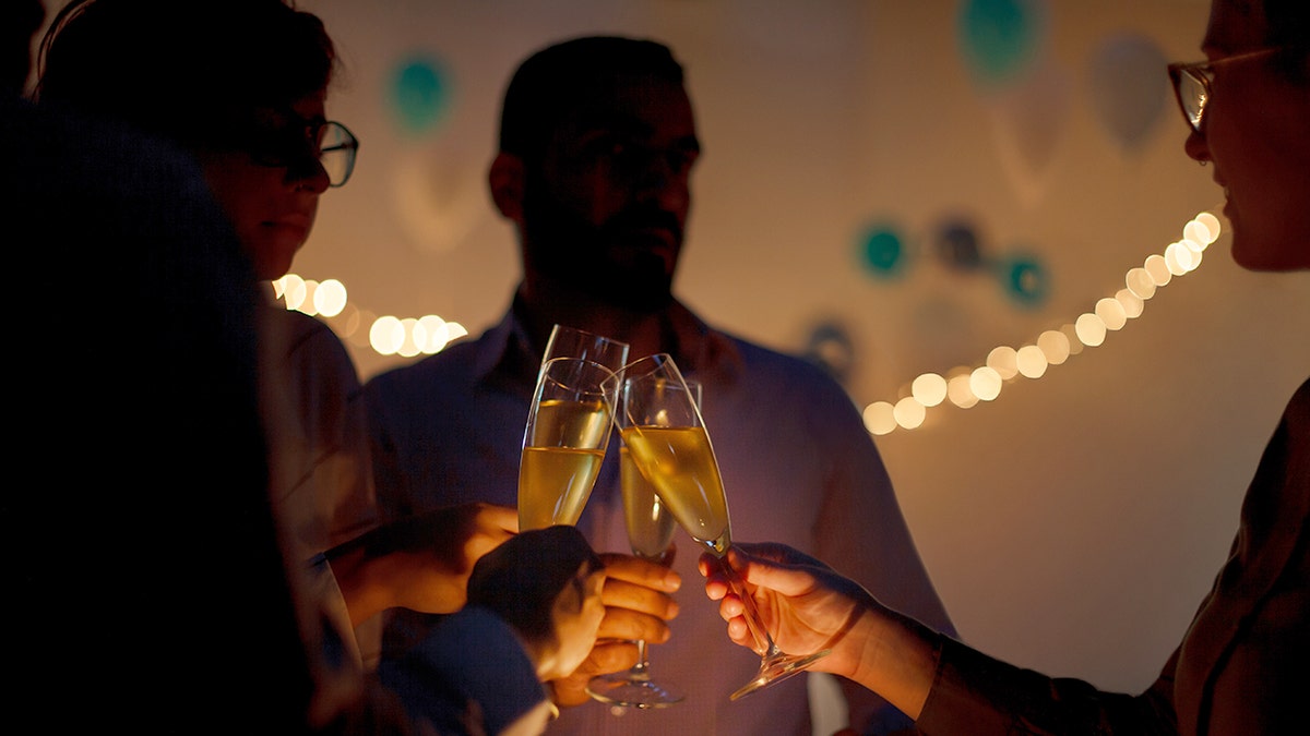 A group of friends in shadow silhouette have champagne glass celebratory toast together