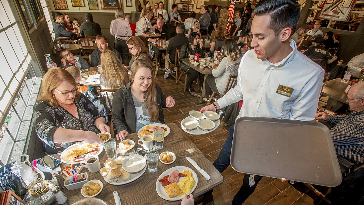 A Cracker Barrel Old Country Store waiter holds a plate near a table inside the restaurant.
