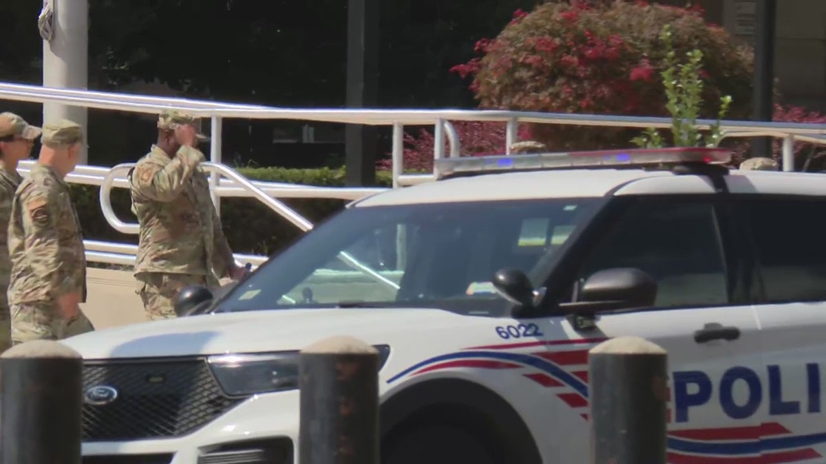 National Guard soldiers walking near a Washington D.C., police vehicle.