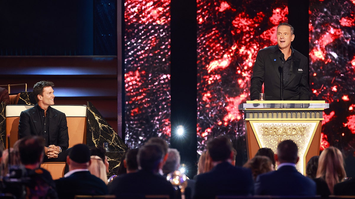 Drew Bledsoe speaks on stage as Tom Brady watches